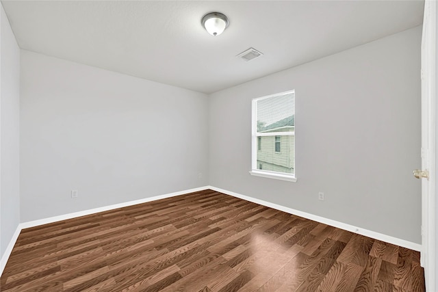 empty room featuring dark wood-type flooring, visible vents, and baseboards