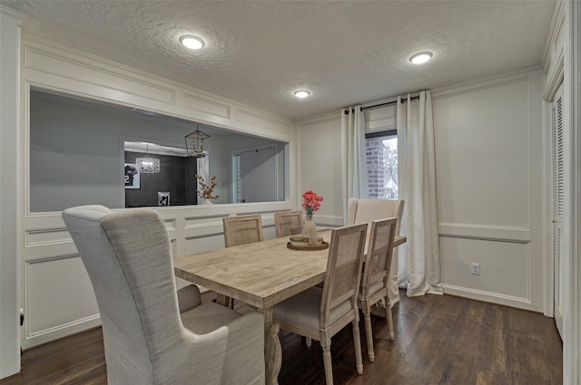 dining room with a textured ceiling, ornamental molding, dark wood-style flooring, and a decorative wall