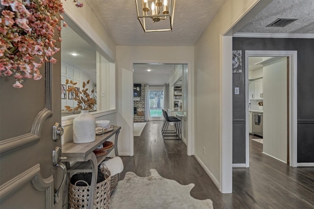 entryway featuring a textured ceiling, a chandelier, visible vents, baseboards, and dark wood-style floors