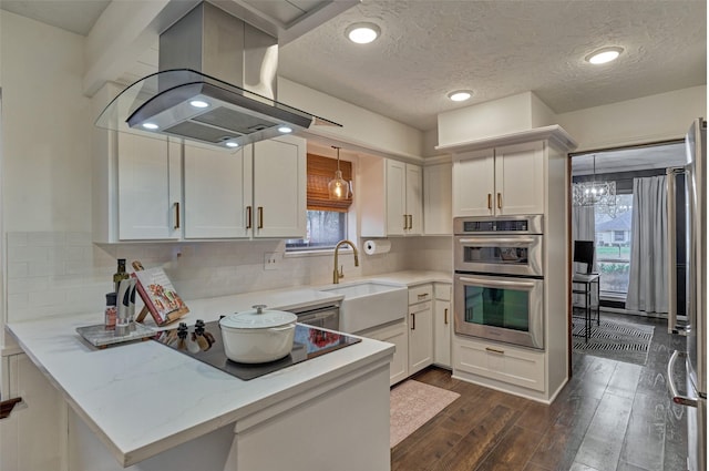 kitchen with a peninsula, double oven, white cabinetry, and island range hood