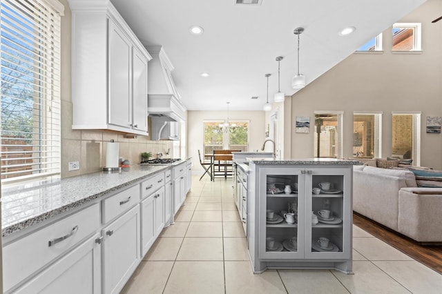 kitchen with hanging light fixtures, glass insert cabinets, open floor plan, white cabinetry, and light stone countertops