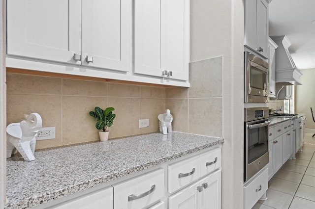 kitchen with light tile patterned floors, tasteful backsplash, appliances with stainless steel finishes, light stone countertops, and white cabinetry