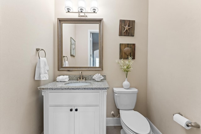 half bathroom with baseboards, vanity, and toilet