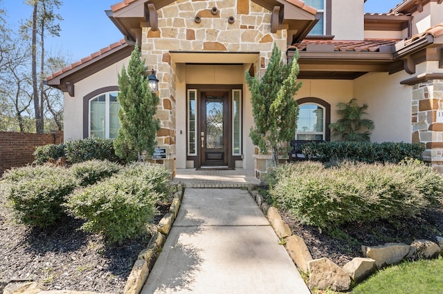 property entrance with stone siding, a tile roof, and stucco siding