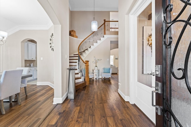 foyer entrance featuring dark wood-style floors, arched walkways, crown molding, baseboards, and stairs