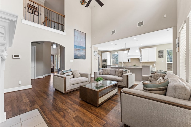 living area with arched walkways, dark wood-style flooring, visible vents, a ceiling fan, and baseboards