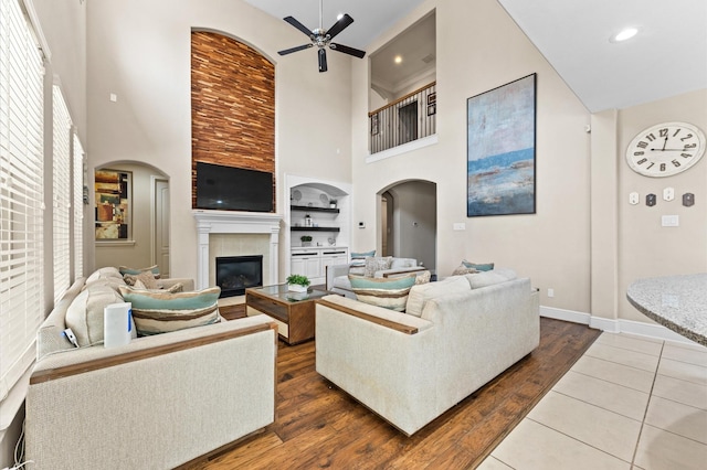 living room featuring a ceiling fan, arched walkways, a fireplace, and wood finished floors