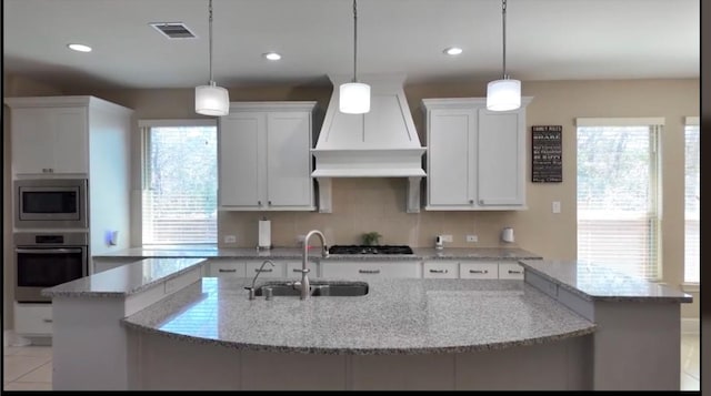 kitchen with appliances with stainless steel finishes, white cabinetry, a sink, and light stone counters