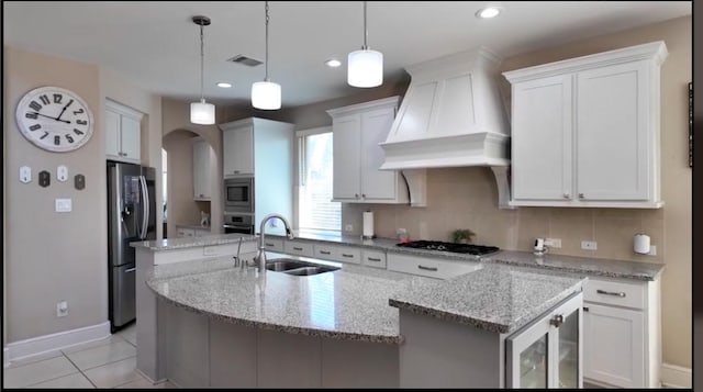 kitchen with decorative light fixtures, appliances with stainless steel finishes, a kitchen island with sink, a sink, and premium range hood