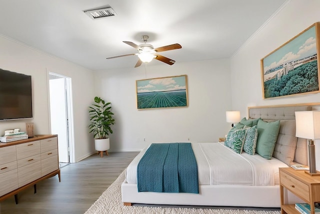 bedroom with crown molding, visible vents, a ceiling fan, wood finished floors, and baseboards