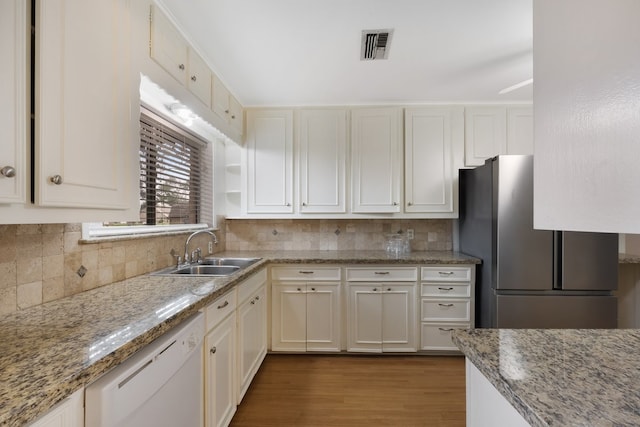 kitchen featuring light stone counters, freestanding refrigerator, white cabinets, white dishwasher, and a sink