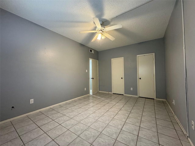 unfurnished room with ceiling fan, light tile patterned floors, a textured ceiling, visible vents, and baseboards