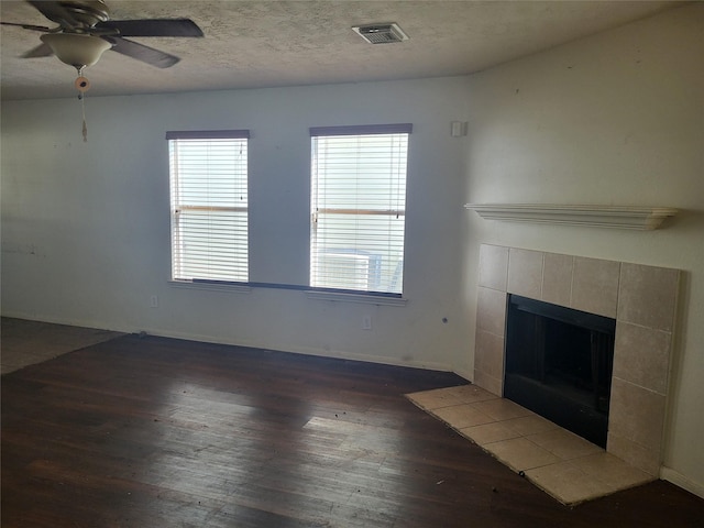 unfurnished living room featuring a textured ceiling, a fireplace, visible vents, a ceiling fan, and dark wood-style floors