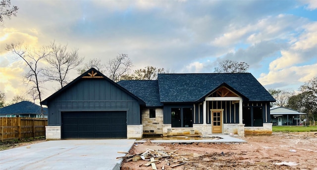 view of front of property with board and batten siding, stone siding, fence, and a garage