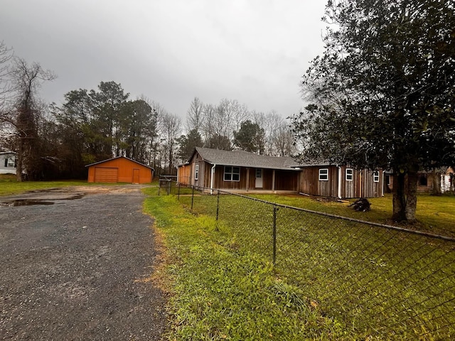 view of front of home featuring driveway, a detached garage, fence, an outdoor structure, and a front lawn