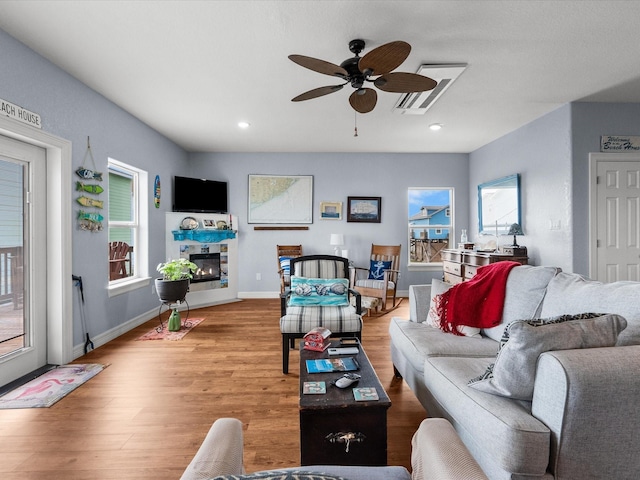 living area with baseboards, a glass covered fireplace, ceiling fan, wood finished floors, and recessed lighting