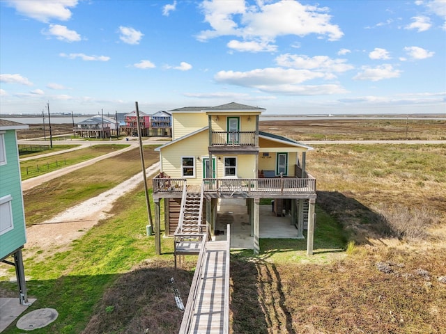 beach home featuring a patio, a balcony, stairs, driveway, and a wooden deck