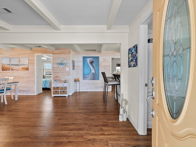foyer entrance with visible vents, dark wood-type flooring, beam ceiling, and wooden walls