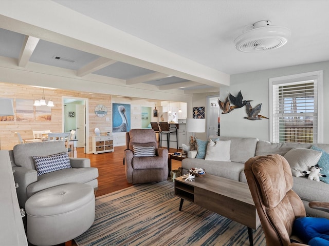 living room featuring beam ceiling, visible vents, an inviting chandelier, wood walls, and wood finished floors