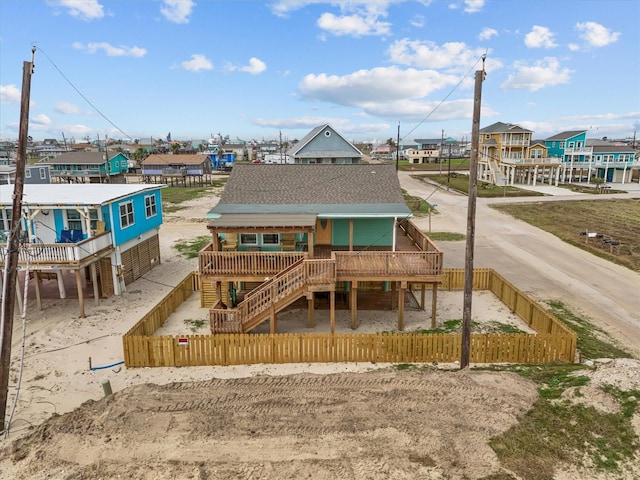 back of house with a fenced front yard, a residential view, stairway, and roof with shingles