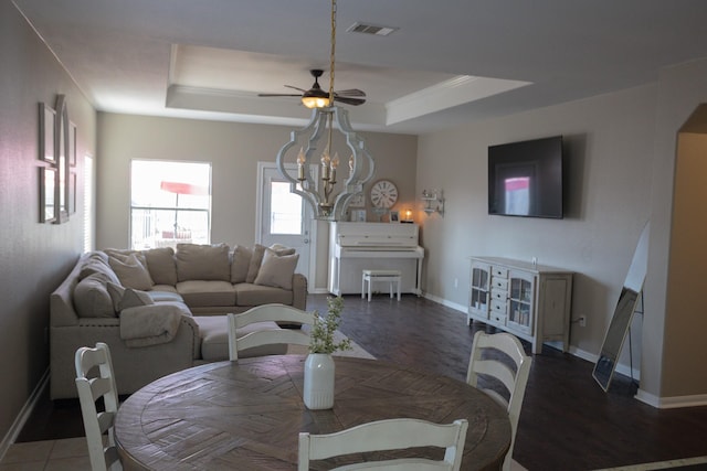 dining space with a tray ceiling, visible vents, baseboards, and ceiling fan with notable chandelier