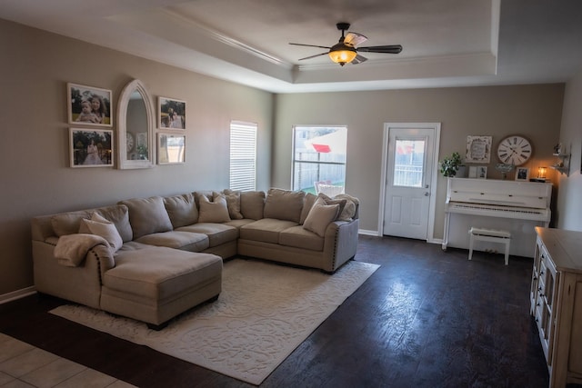 living area with baseboards, dark wood finished floors, a ceiling fan, a tray ceiling, and crown molding