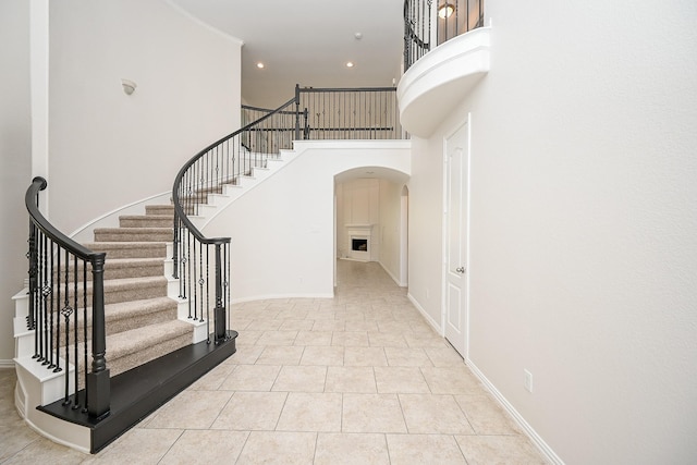 foyer with arched walkways, light tile patterned floors, a towering ceiling, and baseboards