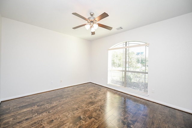 empty room featuring dark wood-style floors, visible vents, ceiling fan, and baseboards