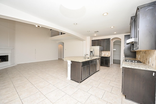 kitchen featuring an island with sink, arched walkways, open floor plan, and a sink