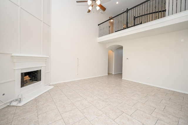 unfurnished living room with a fireplace with raised hearth, arched walkways, a ceiling fan, and baseboards