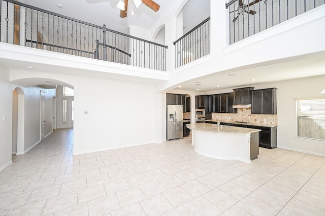 kitchen with tasteful backsplash, a center island with sink, a ceiling fan, light stone counters, and stainless steel appliances