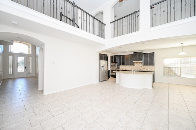 unfurnished living room featuring arched walkways, light tile patterned flooring, a towering ceiling, and baseboards