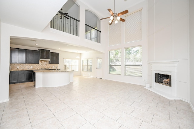 unfurnished living room featuring light tile patterned floors, baseboards, a fireplace with raised hearth, a ceiling fan, and recessed lighting