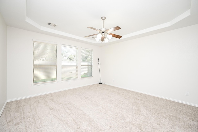 spare room with light carpet, visible vents, a ceiling fan, baseboards, and a raised ceiling