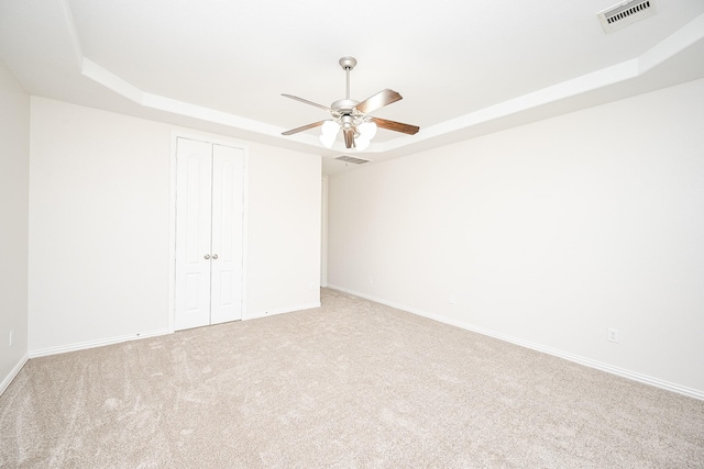 unfurnished bedroom featuring visible vents, a tray ceiling, a closet, and carpet flooring