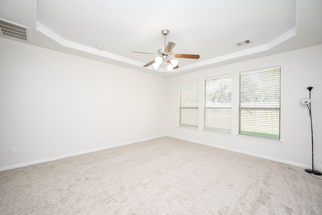 carpeted spare room with visible vents, a tray ceiling, and baseboards