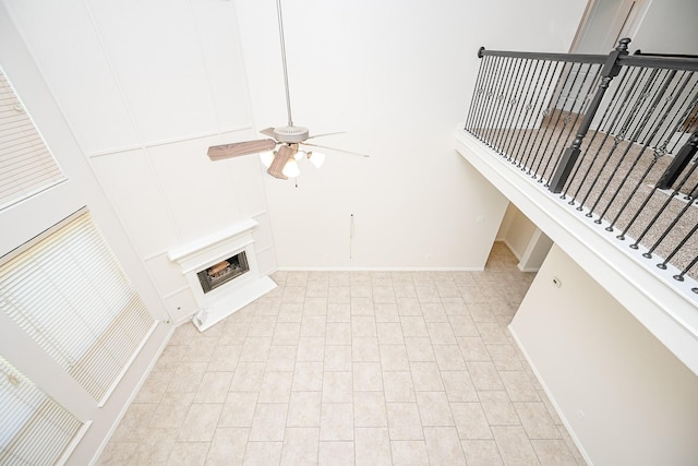 unfurnished living room with baseboards, a fireplace with raised hearth, ceiling fan, stairway, and a high ceiling