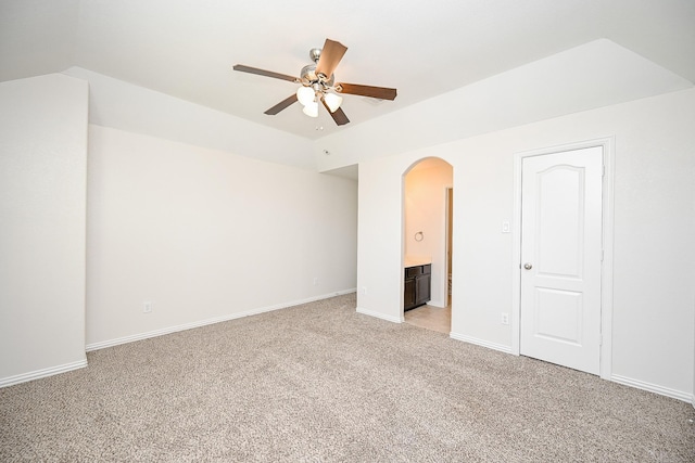 unfurnished bedroom with arched walkways, lofted ceiling, light carpet, baseboards, and ensuite bath