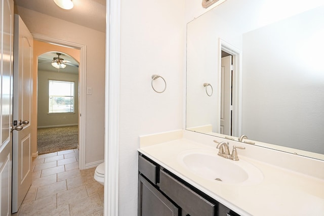 half bathroom with tile patterned flooring, toilet, a ceiling fan, vanity, and baseboards