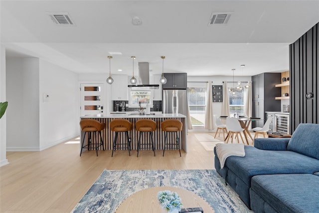 living area with a chandelier, light wood finished floors, visible vents, and baseboards