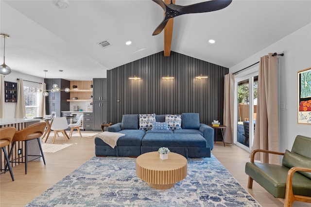 living area with an accent wall, a wealth of natural light, ceiling fan, and lofted ceiling with beams