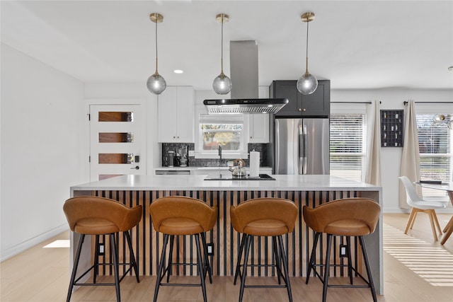 kitchen with a large island, decorative light fixtures, freestanding refrigerator, range hood, and light countertops