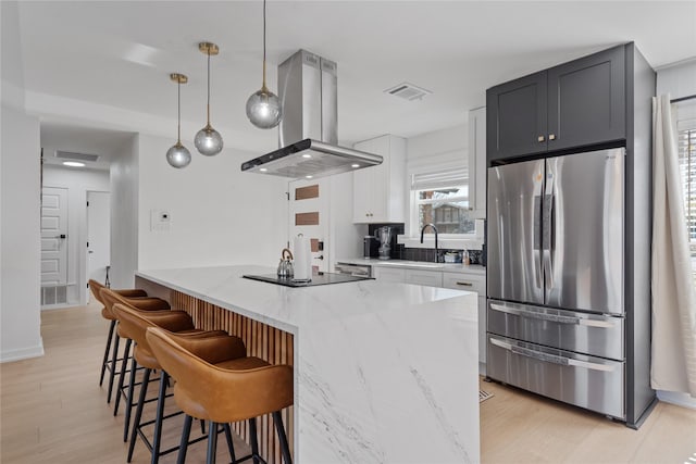 kitchen featuring light stone counters, decorative light fixtures, freestanding refrigerator, island exhaust hood, and white cabinetry