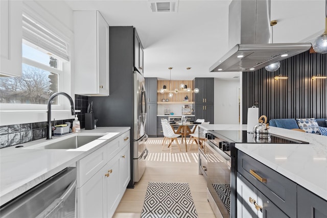 704 Emerald Wood Dr, Austin, TX 78745 - kitchen featuring appliances with stainless steel finishes, a sink, island range hood, white cabinetry, and decorative light fixtures