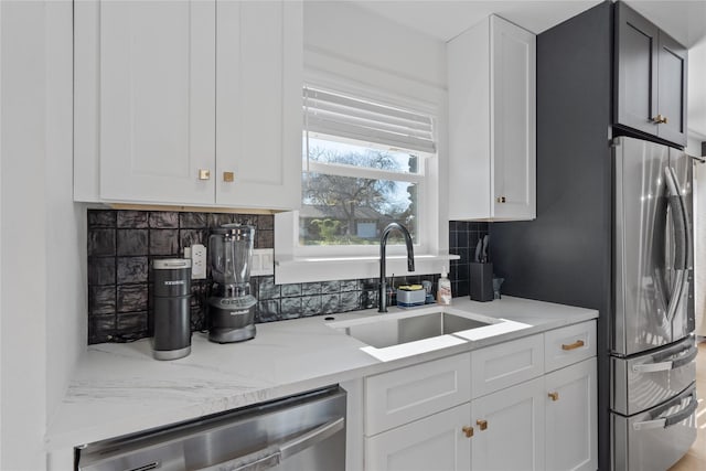 kitchen featuring stainless steel appliances, tasteful backsplash, white cabinetry, a sink, and light stone countertops