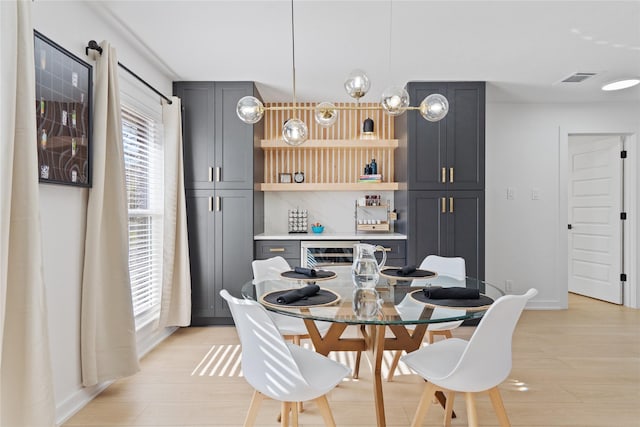 dining area with baseboards, visible vents, a bar, and light wood finished floors