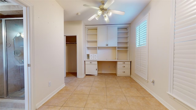 unfurnished bedroom with built in desk, two closets, light tile patterned flooring, ceiling fan, and baseboards