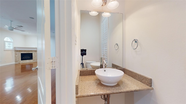 bathroom with a ceiling fan, a fireplace, a sink, and wood finished floors