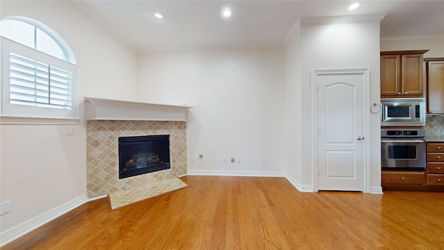 unfurnished living room with light wood-type flooring, crown molding, baseboards, and a tiled fireplace