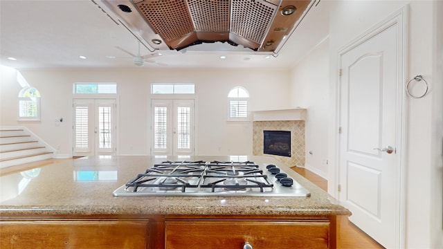 kitchen with a glass covered fireplace, open floor plan, light stone countertops, french doors, and gas cooktop